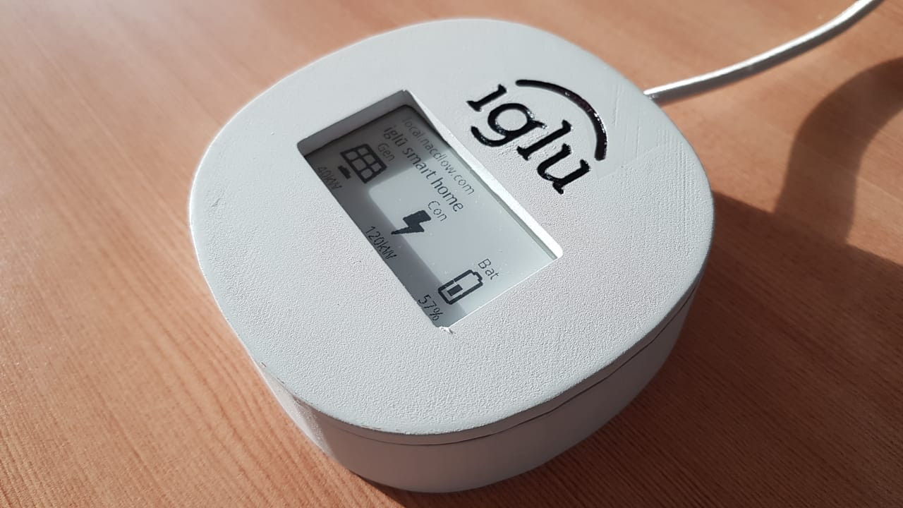 a photograph of the iglü device, which is a 3D printed rounded box with an e-ink display, showing the URL of the system at local.nacdlow.com, the power generation as 40 kilowatts, the power consumption at 120 kilowatts, and the battery level at 57%